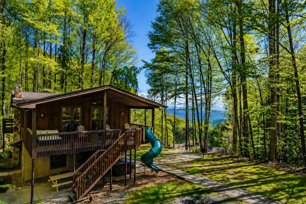 Modern cabin with deck and slide nestled among tall trees with mountain views in background